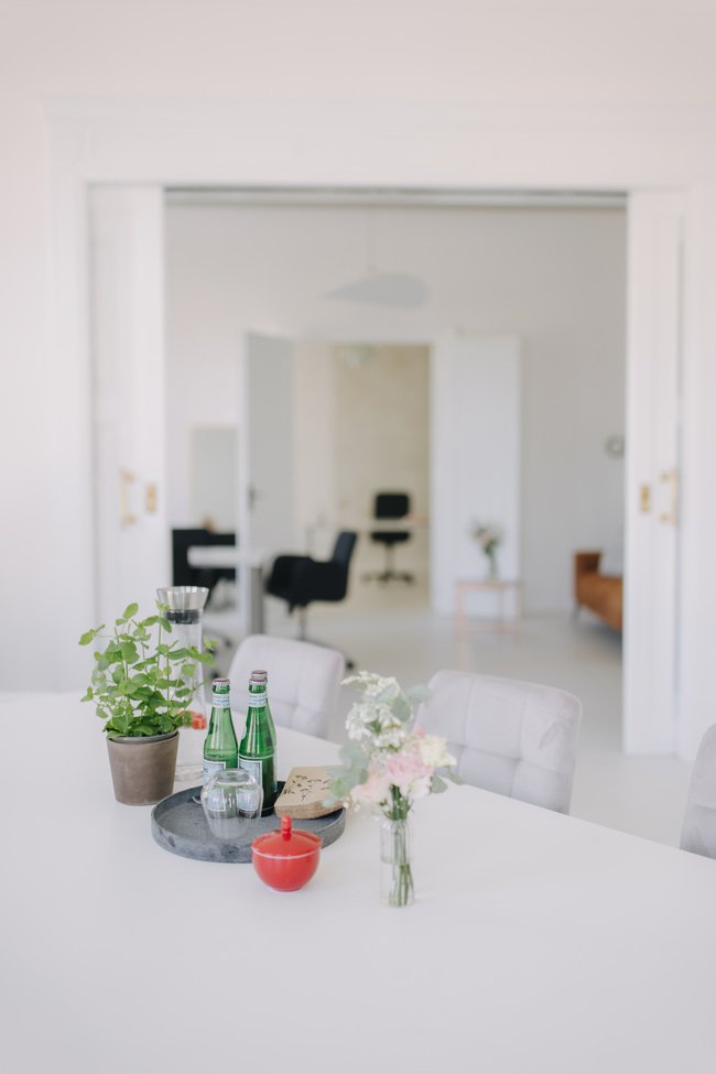 Minimalistisch eingerichteter Raum mit gedecktem Tisch, Pflanzen, Blumen und Getränken, modern und einladend gestaltet.