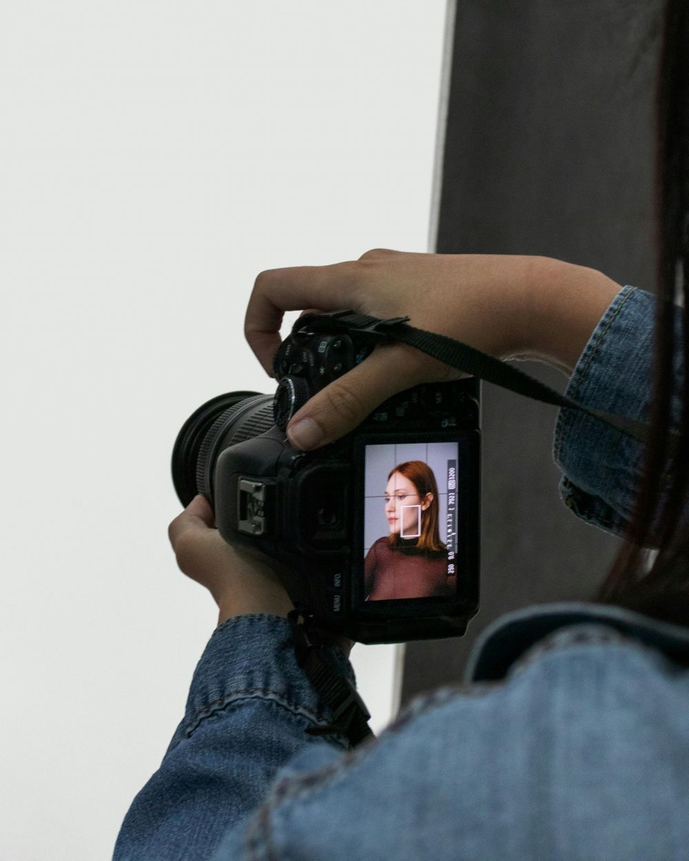 Das Bild zeigt eine Fotografin, die mit einer Kamera ein Porträt aufnimmt. Der Kamerabildschirm zeigt eine Frau im Fokus.