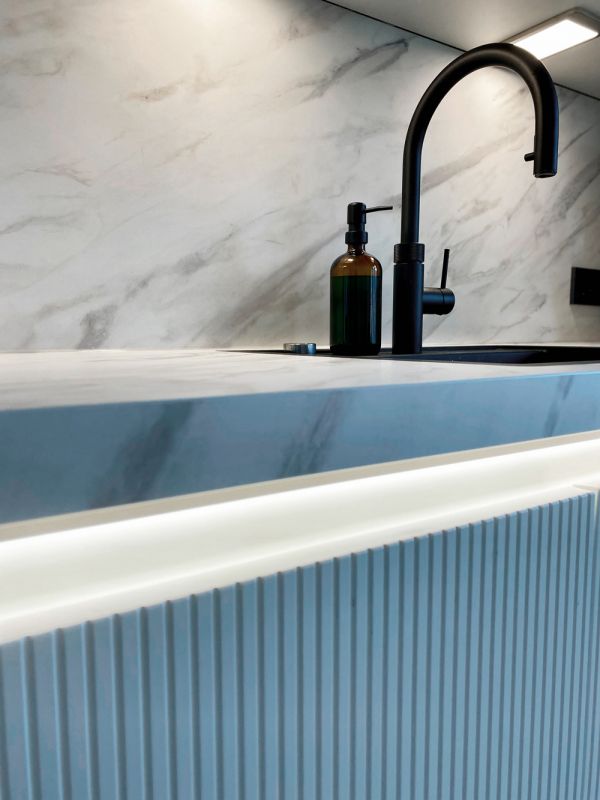 Detail einer modernen Küchenzeile mit Marmoroptik, schwarzer Armatur, LED-Beleuchtung und stilvoll geriffelter Front.