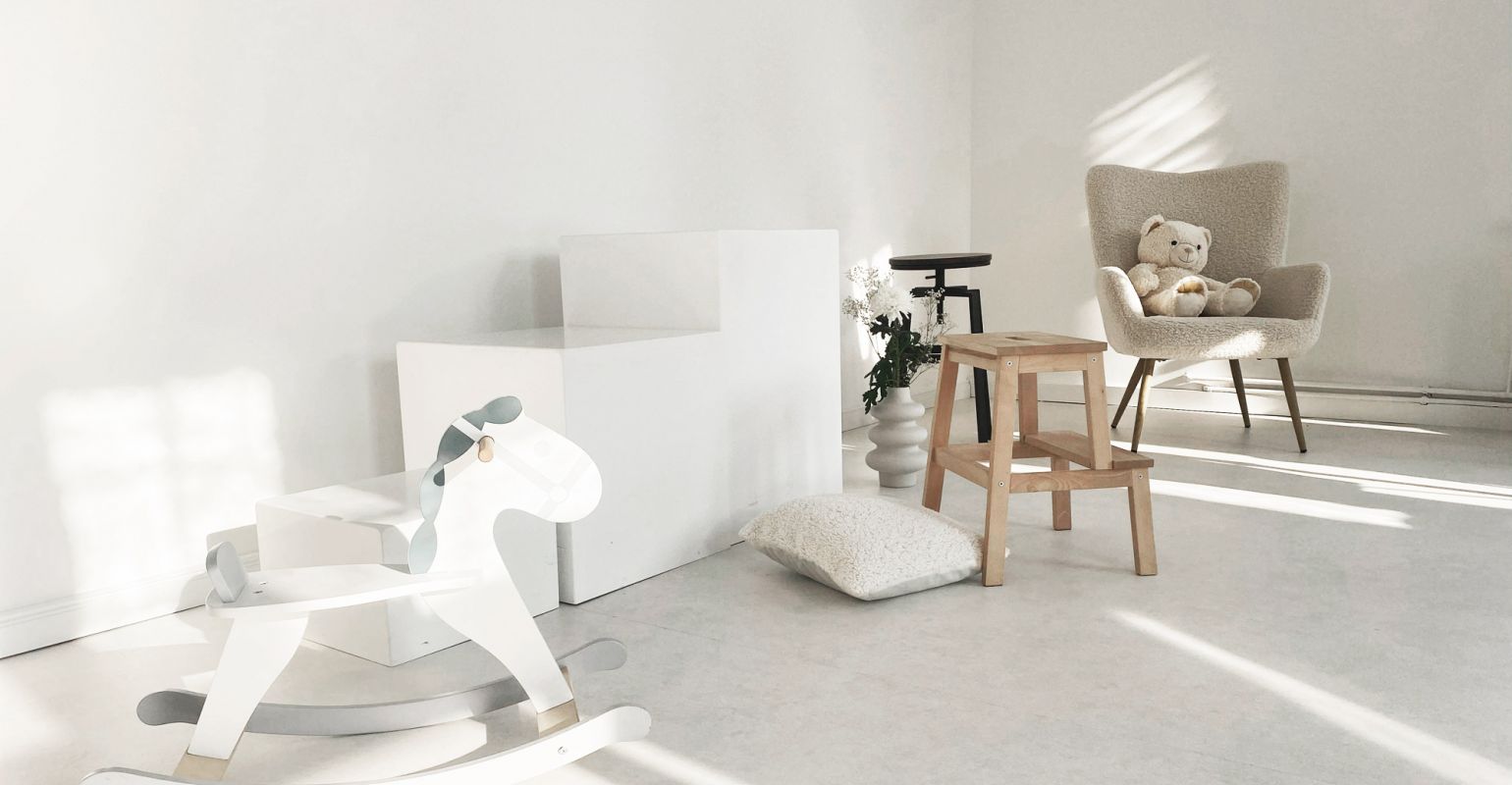 Heller Raum mit skandinavischem Design, Kinder-Schaukelpferd, Holzstuhl, Teddy auf Sessel und minimalistischem Dekor.