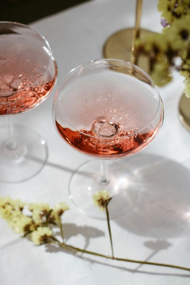 Zwei Gläser Rosé-Sekt auf elegantem Tisch, dekoriert mit Blumen und goldenen Akzenten, stilvoll und festlich arrangiert.