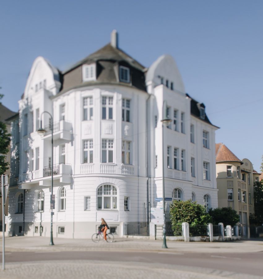 Stilvolles historisches Gebäude mit weißen Fassaden an einer Straßenecke, bei sonnigem Wetter.