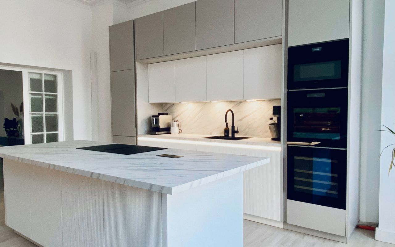 Moderne Küche mit Kücheninsel in Marmoroptik, eingebauter Beleuchtung, schwarzen Geräten und minimalistischem Design.