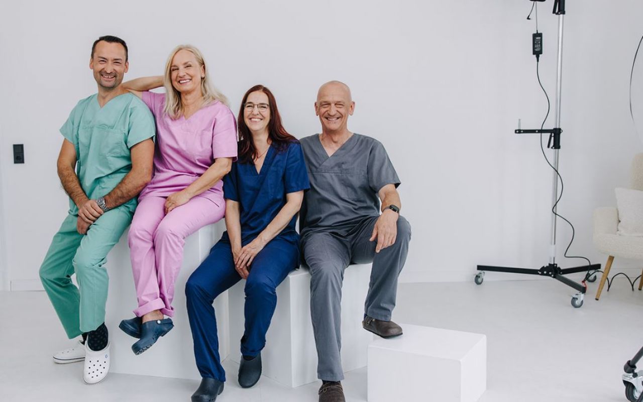 Gruppe von Ärzten und Pflegekräften in bunter Arbeitskleidung, lächelnd in einem modernen, hellen Studio für Teamfotos.